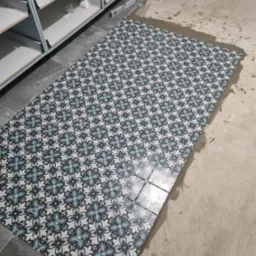 Układanie wzorzystych płytek podłogowych w trakcie remontu, widoczny poziomica, krzyżyki dystansowe i wiadro z zaprawą.