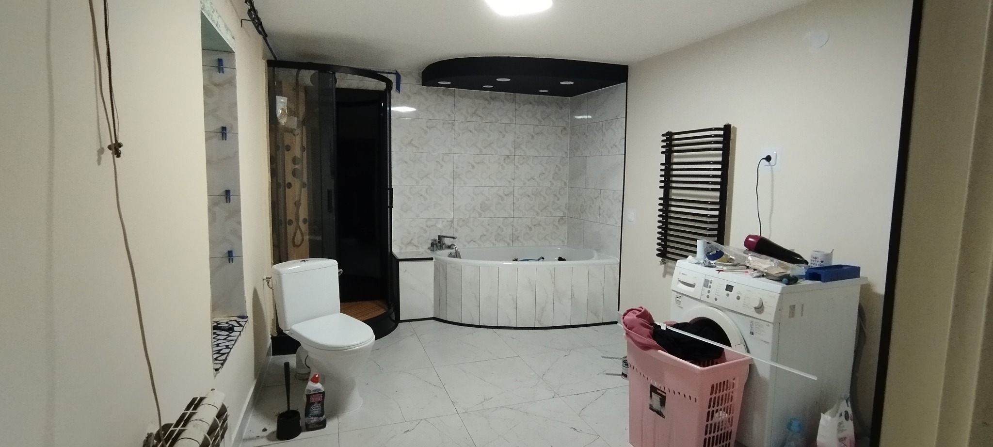 Ukończona łazienka w Ostrowie Wielkopolskim z wanną narożną, kabiną prysznicową i toaletą, widoczna pralka z akcesoriami na górze, sugerująca dalsze prace wykończeniowe.