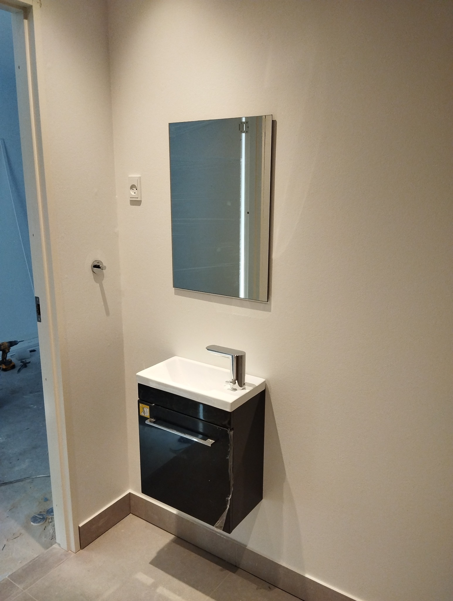 Nowoczesna umywalka z szafką w kolorze czarnym i lustrem w łazience, widoczne narzędzia i niedokończone prace wykończeniowe.