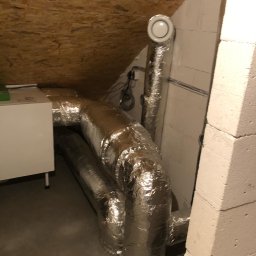 Kosmala - Srebrne rury wentylacyjne w izolacji termicznej poprowadzone w przestrzeni poddasza, widoczny fragment rekuperatora.