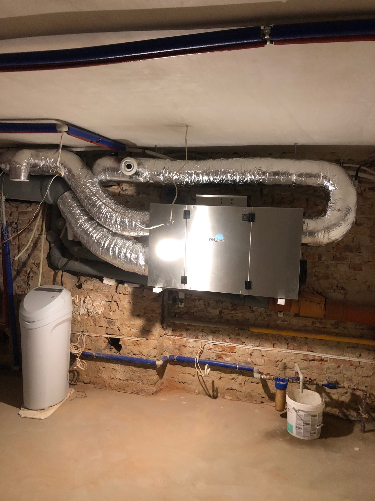 Zainstalowana centrala rekuperacyjna reQnet z izolowanymi przewodami wentylacyjnymi w pomieszczeniu z ceglanymi ścianami i widocznymi instalacjami.