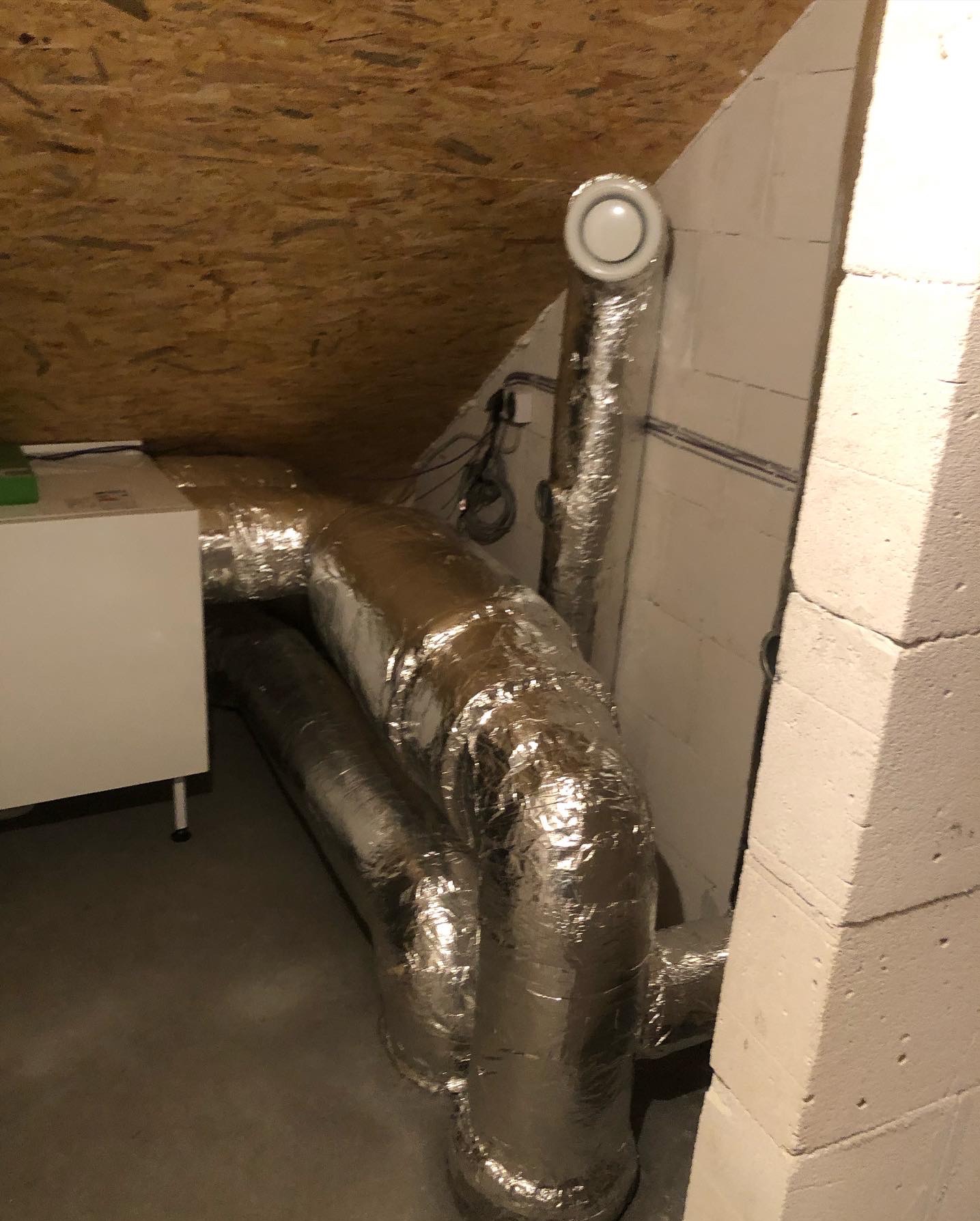 Srebrne rury wentylacyjne w izolacji termicznej poprowadzone w przestrzeni poddasza, widoczny fragment rekuperatora.