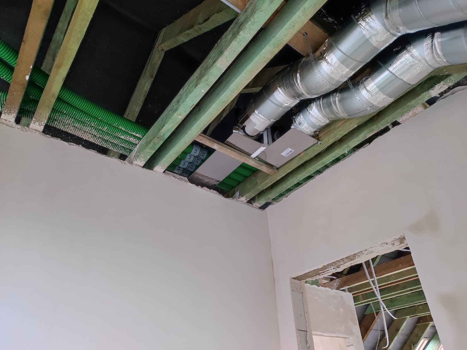 Montaż instalacji wentylacyjnej w domu: widoczne zielone rury wentylacyjne pod sufitem i srebrne rury w izolacji, ukazujące zaawansowany etap prac.