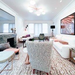 Fajny Elektryk Maciej Karaś - Elegancki salon z marmurowym kominkiem, nowoczesnym oświetleniem sufitowym i dywanem w geometryczne wzory, widziany zza fotela w szarej tkaninie.