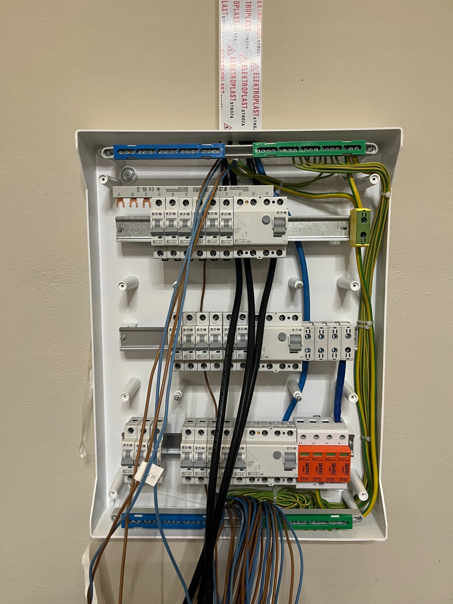 Rozdzielnica elektryczna z zainstalowanymi bezpiecznikami EATON, listwami zaciskowymi i przewodami w kolorach: czarnym, brązowym, niebieskim, zielono-żółtym oraz pomarańczowy ogranicznik przepięć...