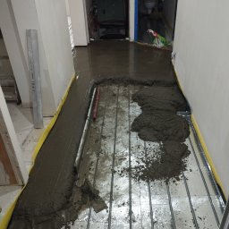 Mateusz Kuleta - Wylewka samopoziomująca rozprowadzana na folii z ogrzewaniem podłogowym, widoczne narzędzia i poziomica.