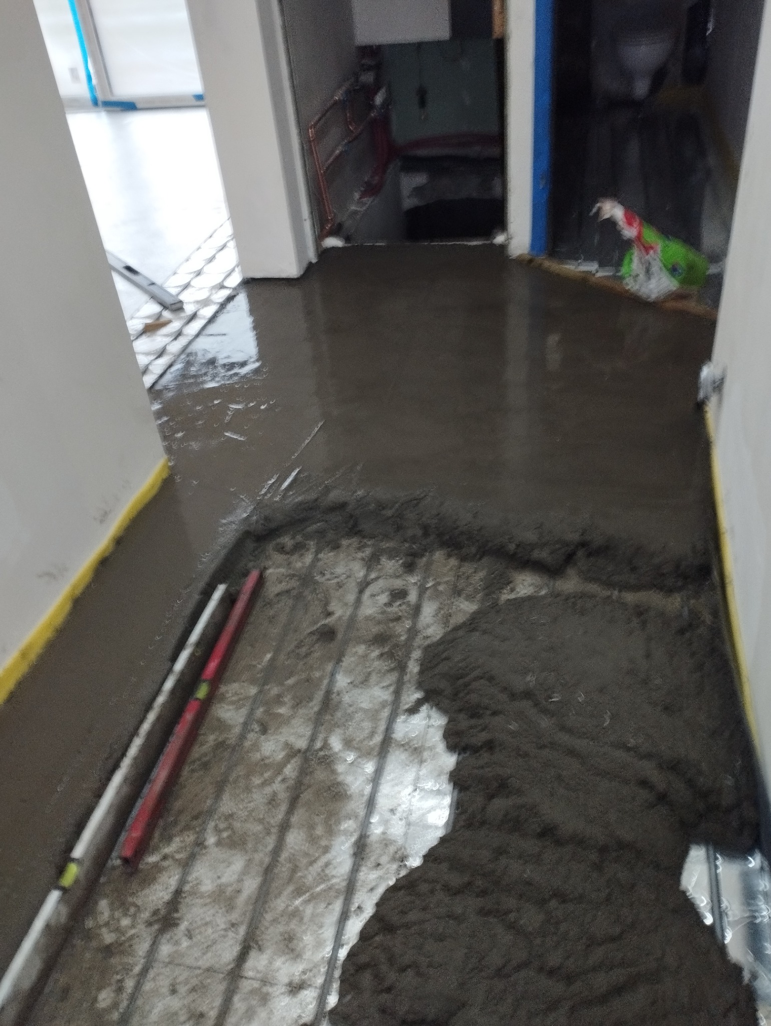 Wylewka samopoziomująca na ogrzewaniu podłogowym w trakcie rozprowadzania, widoczny poziomujący przymiar.