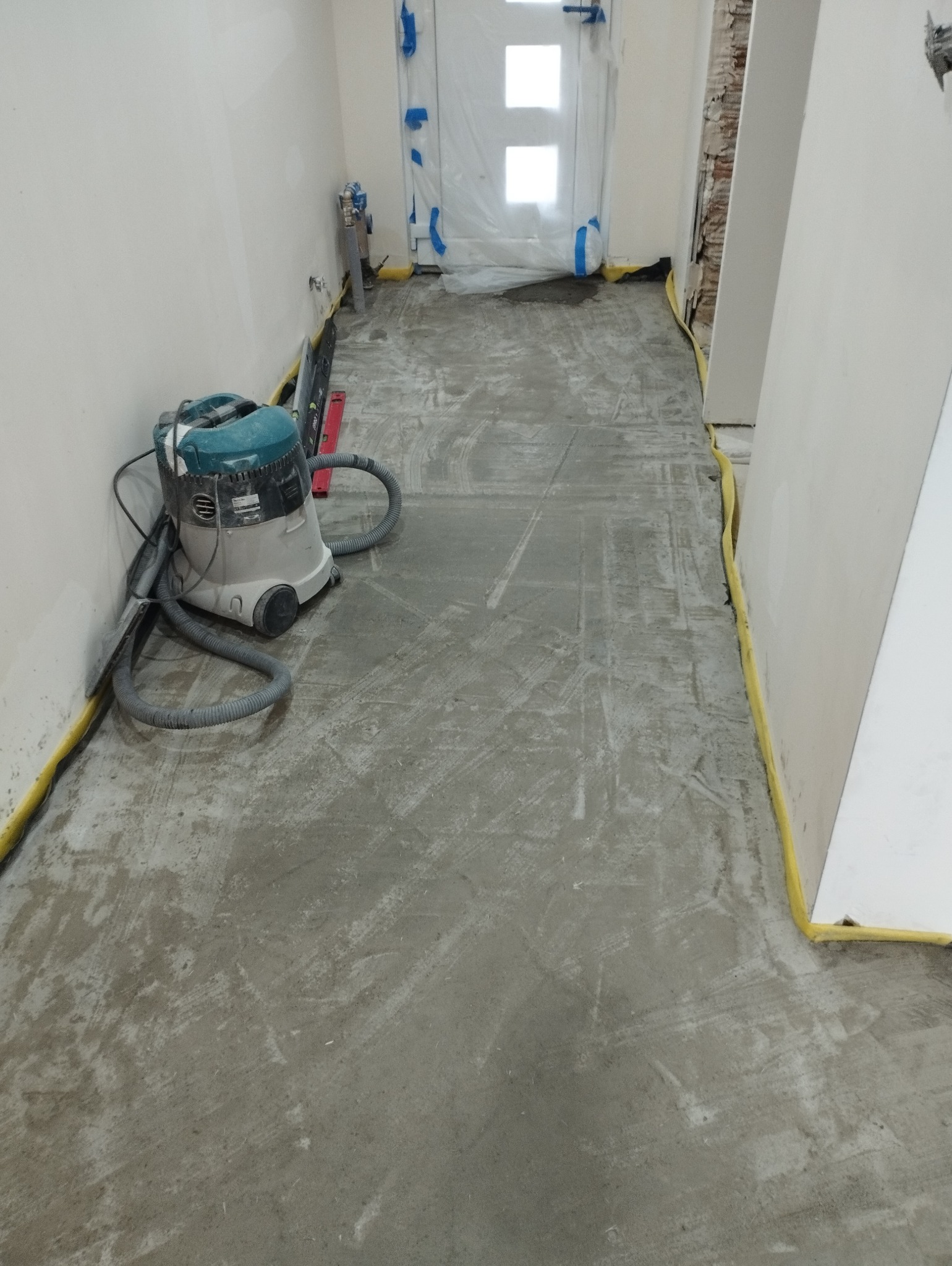 Przygotowanie podłoża: Szlifowana wylewka samopoziomująca w korytarzu, zabezpieczone ściany taśmą malarską, odkurzacz przemysłowy Makita. Widoczne ślady po szlifowaniu.
