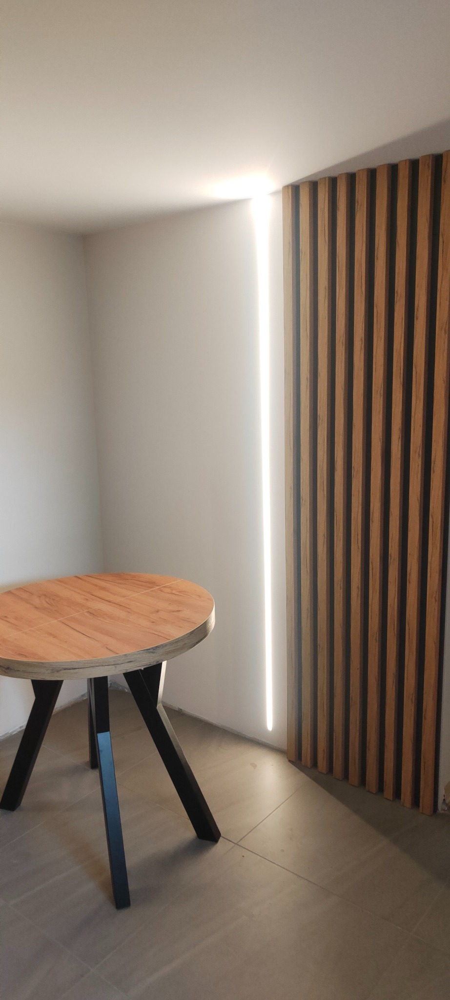 Drewniany stół z czarnymi nogami na tle ściany z drewnianymi panelami i pionowym oświetleniem LED. Nowoczesny design wnętrza.