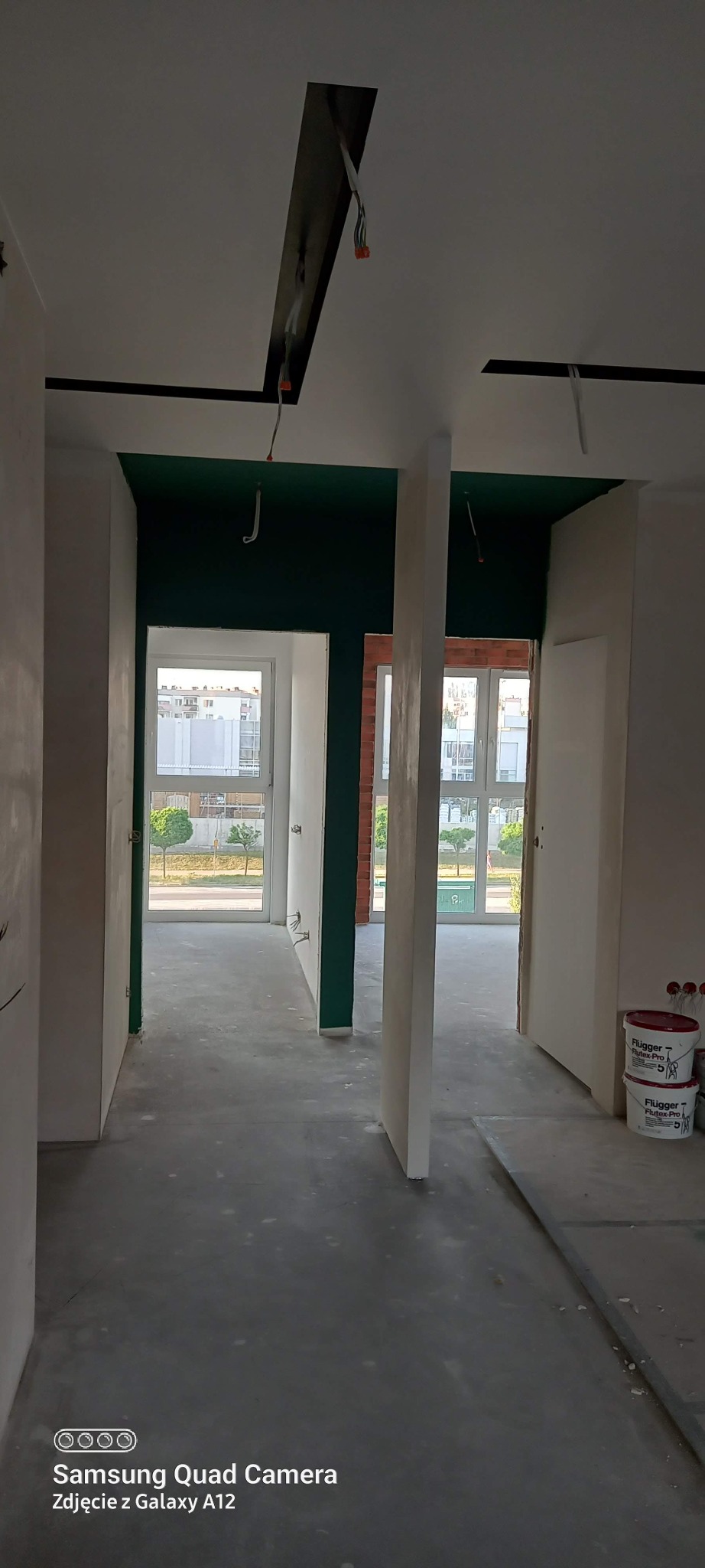 Wnętrze w trakcie wykańczania: pomalowany sufit na zielono, ściany w trakcie gładzenia, widoczne puszki z farbą. Prace wykończeniowe w nowym mieszkaniu.