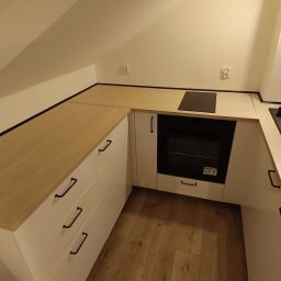 NUD Bud NAZAR HLYNKA - Nowoczesna, jasna kuchnia na poddaszu ze skośnym sufitem. Białe szafki z drewnianym blatem, czarny zlew i bateria. Minimalistyczny design, oświetlenie punktowe.