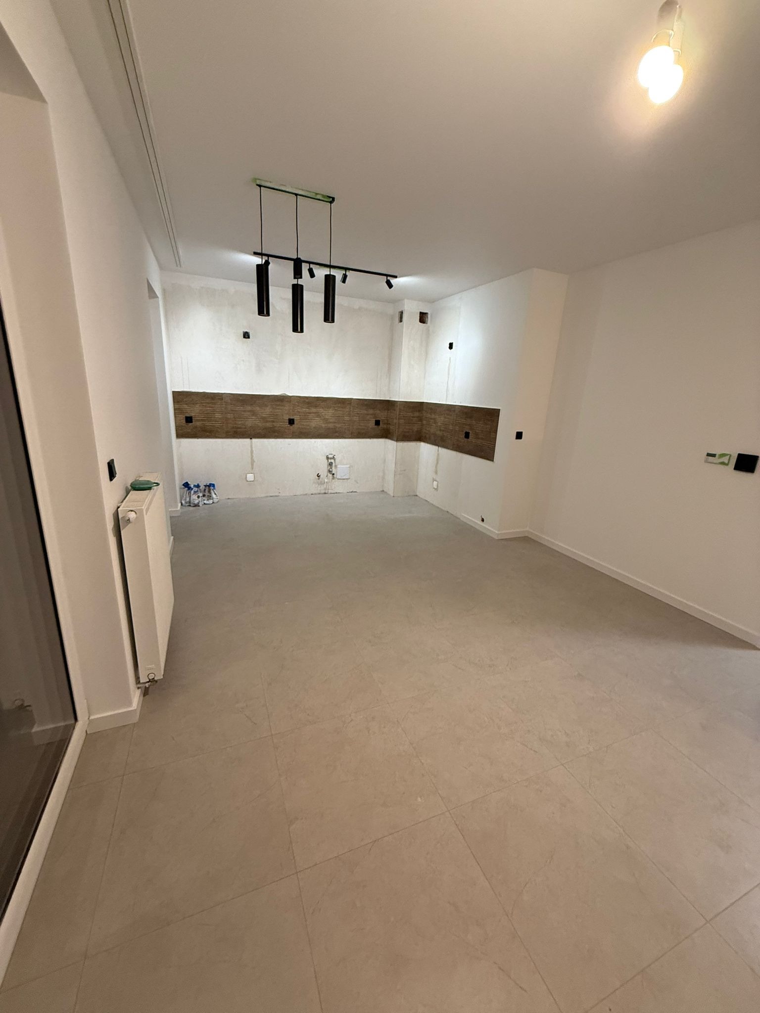 Wnętrze w trakcie wykańczania: beżowa podłoga z płytek, białe ściany z elementami dekoracyjnymi z drewna, nowoczesne oświetlenie sufitowe.