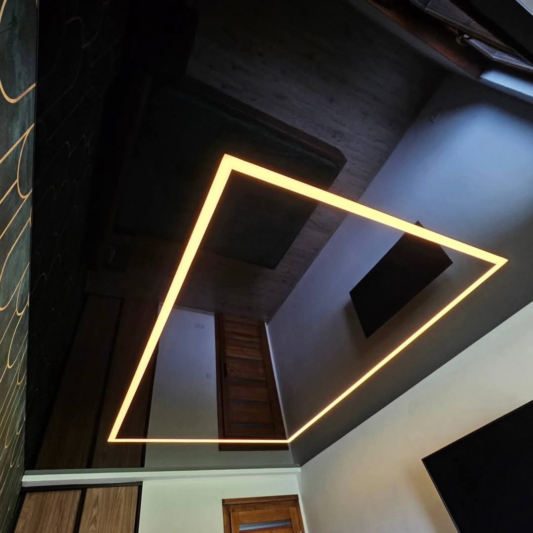 Błyszczący, czarny sufit z efektem lustra, podświetlony kwadratową lampą LED, widoczne odbicie elementów wystroju wnętrza.