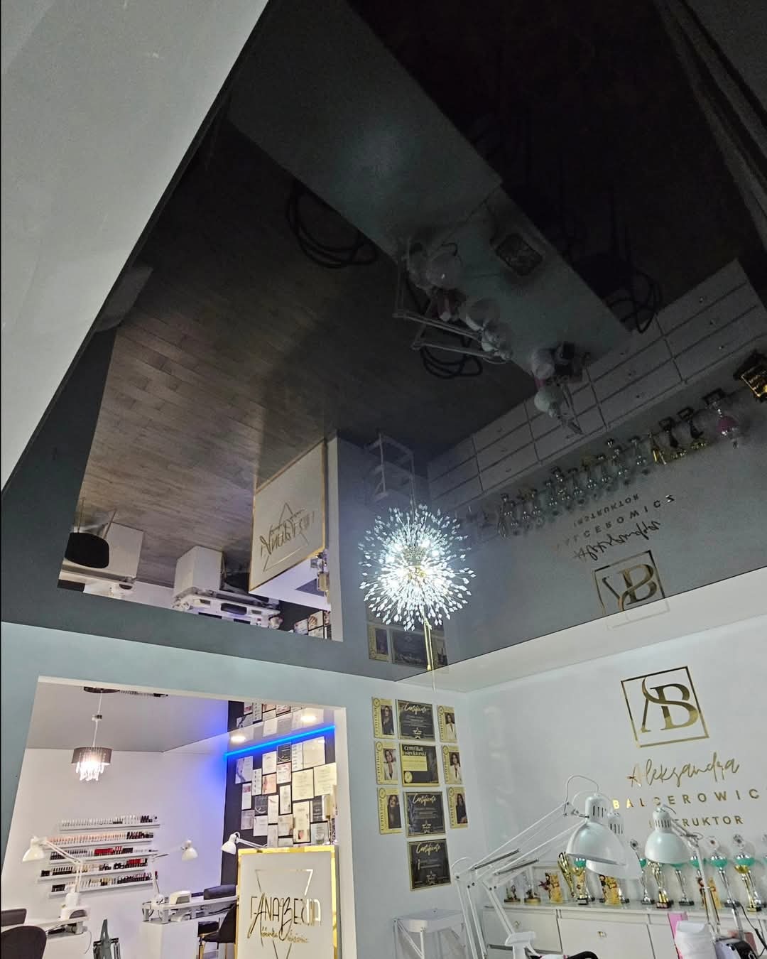 Ciemny, błyszczący sufit odbija wnętrze salonu kosmetycznego z oświetleniem punktowym, widoczne certyfikaty i wyposażenie stanowiska pracy.