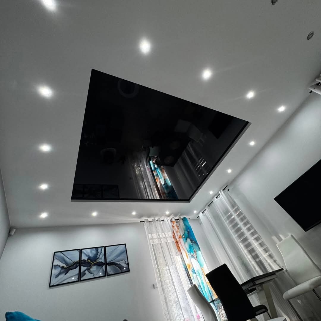 Czarny, lustrzany sufit napinany w kształcie kwadratu z oświetleniem punktowym, odbijający wnętrze salonu z zasłonami i obrazami.