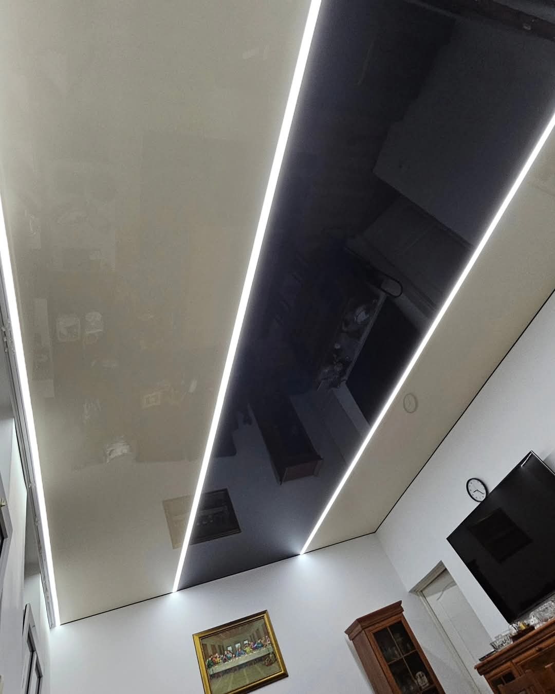 Dwukolorowy sufit z połyskiem, przedzielony liniami LED, odbijający wyposażenie pokoju.
