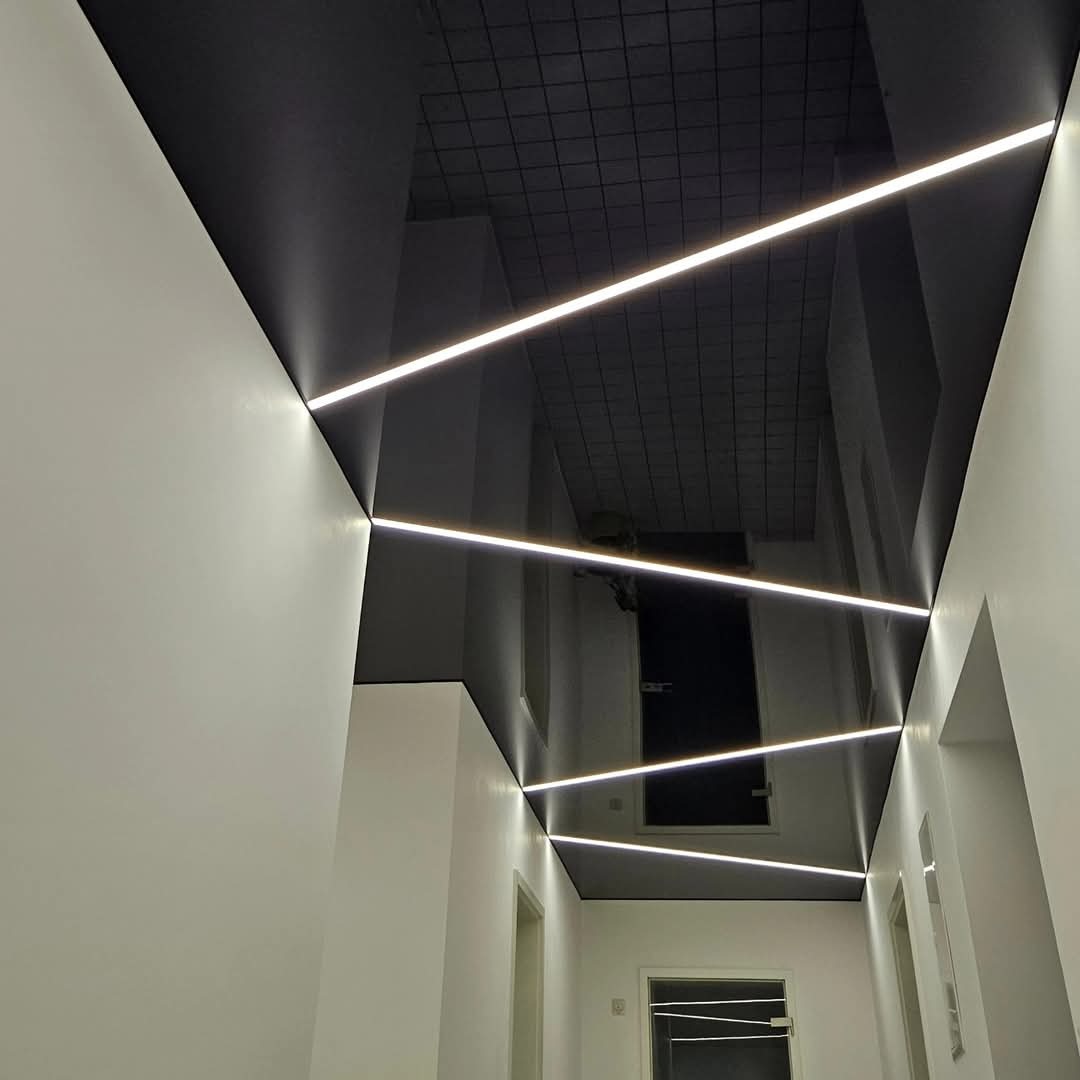 Czarny, błyszczący sufit napinany z trzema liniami oświetlenia LED w korytarzu z białymi ścianami i drzwiami.