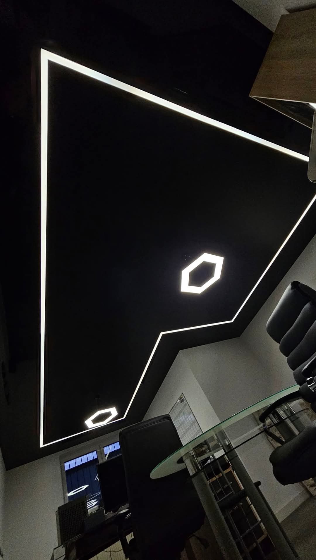 Czarne podwieszane wnętrze biura z geometrycznymi liniami oświetlenia LED, widok z dołu na szklany stół i krzesła biurowe