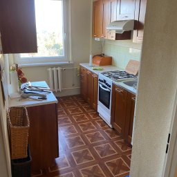 Michał Rostowski - Ustawna kuchnia z drewnianymi szafkami, brązową podłogą w geometryczny wzór i białym piecem, widok zza progu.