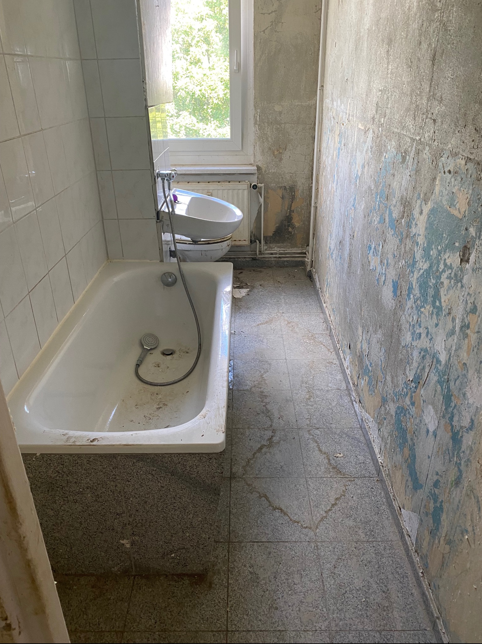 Łazienka w trakcie demontażu: stara wanna, bidet, zniszczone płytki i ściany z resztkami farby, widoczne ślady po zalaniach.