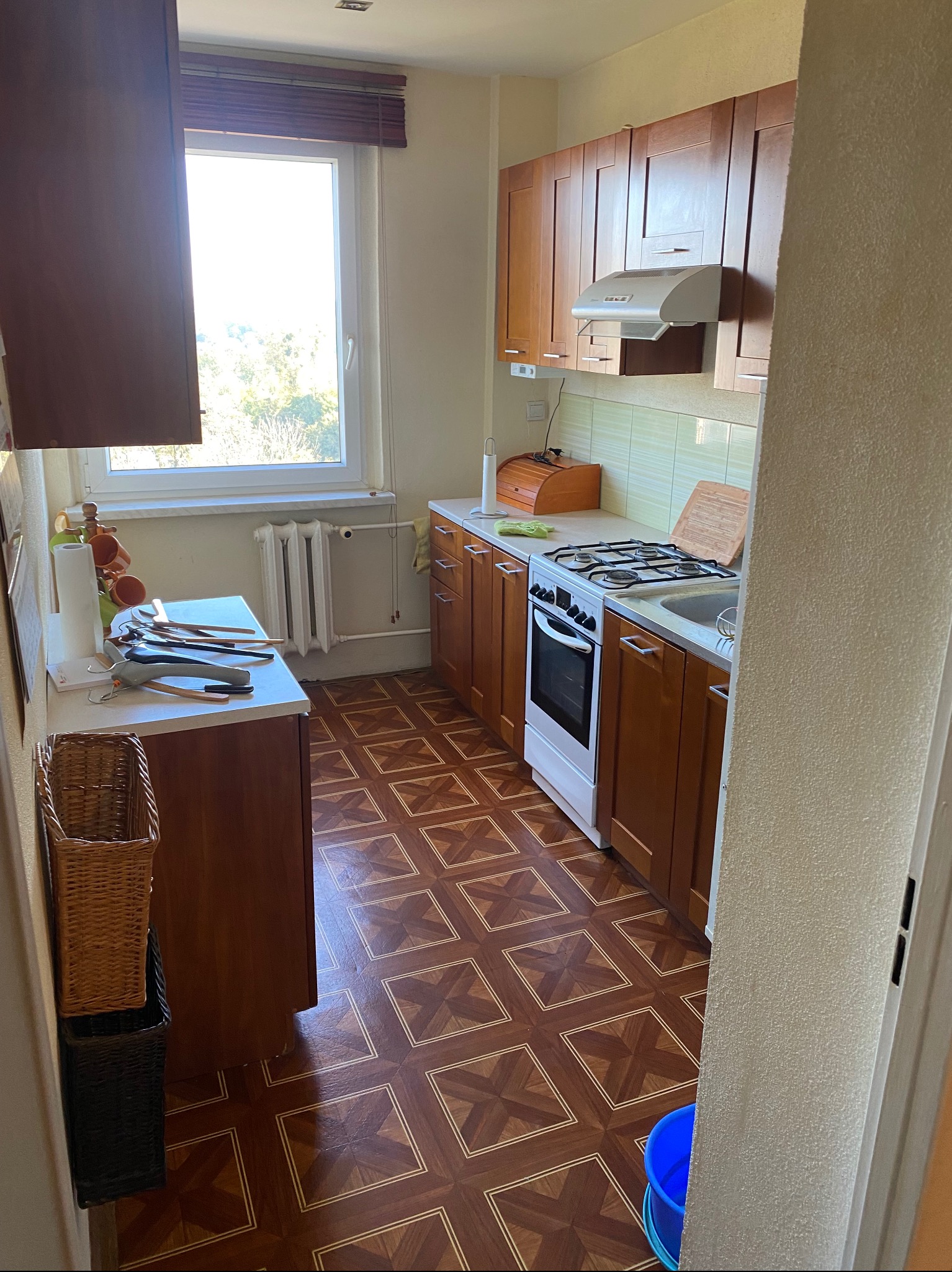 Ustawna kuchnia z drewnianymi szafkami, brązową podłogą w geometryczny wzór i białym piecem, widok zza progu.