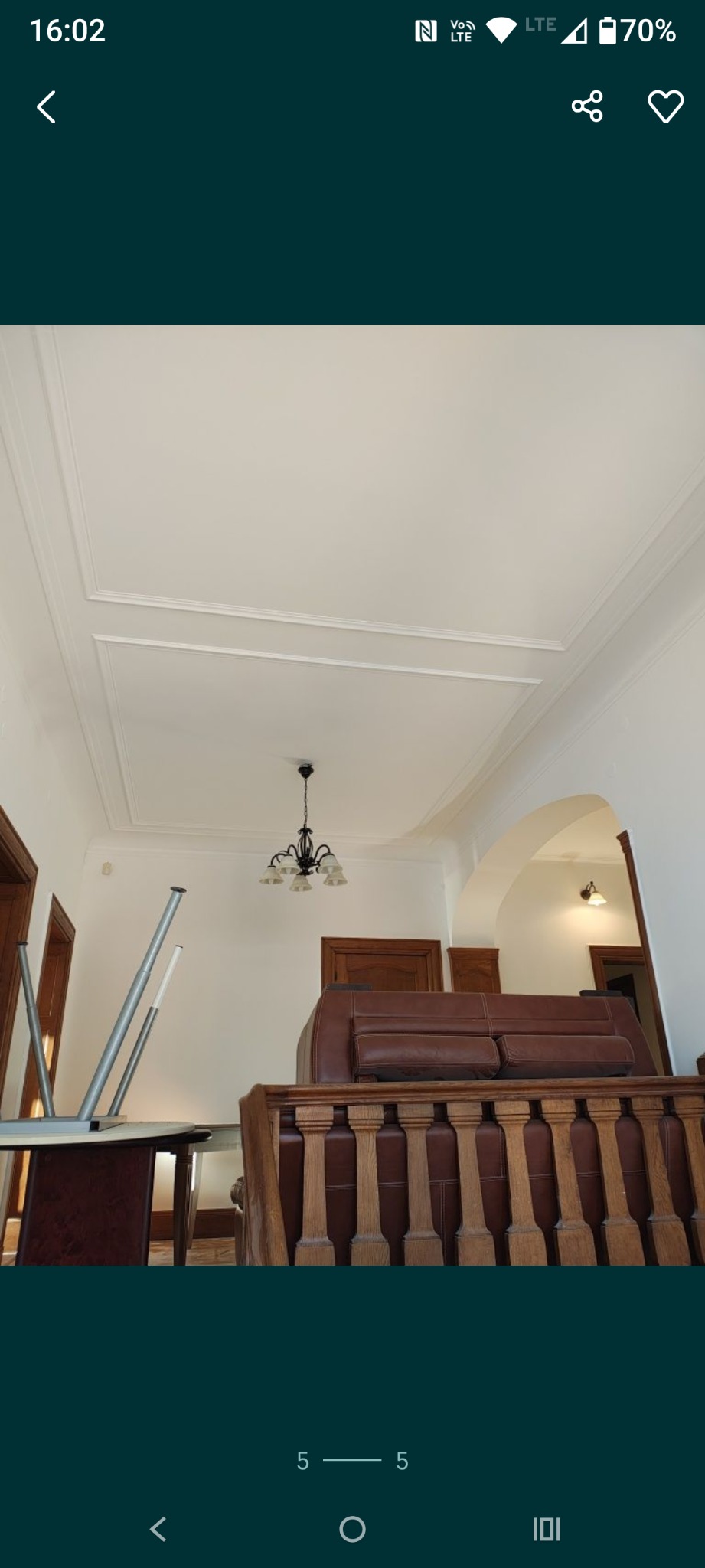 Biały sufit z dekoracyjnymi listwami i wiszącą lampą w odnowionym wnętrzu. Widoczny fragment sofy i odwrócony stół, sugerujący prace wykończeniowe.