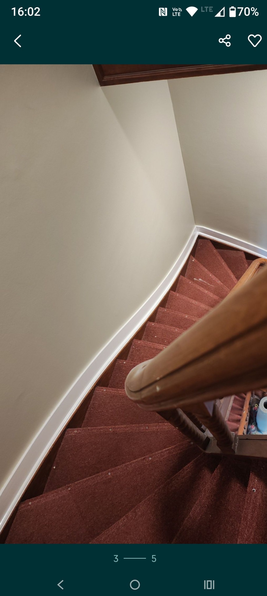 Spiralne schody z bordową wykładziną dywanową i drewnianą balustradą, widok z góry. Ściany pomalowane na jasny odcień beżu z białymi listwami przypodłogowymi.