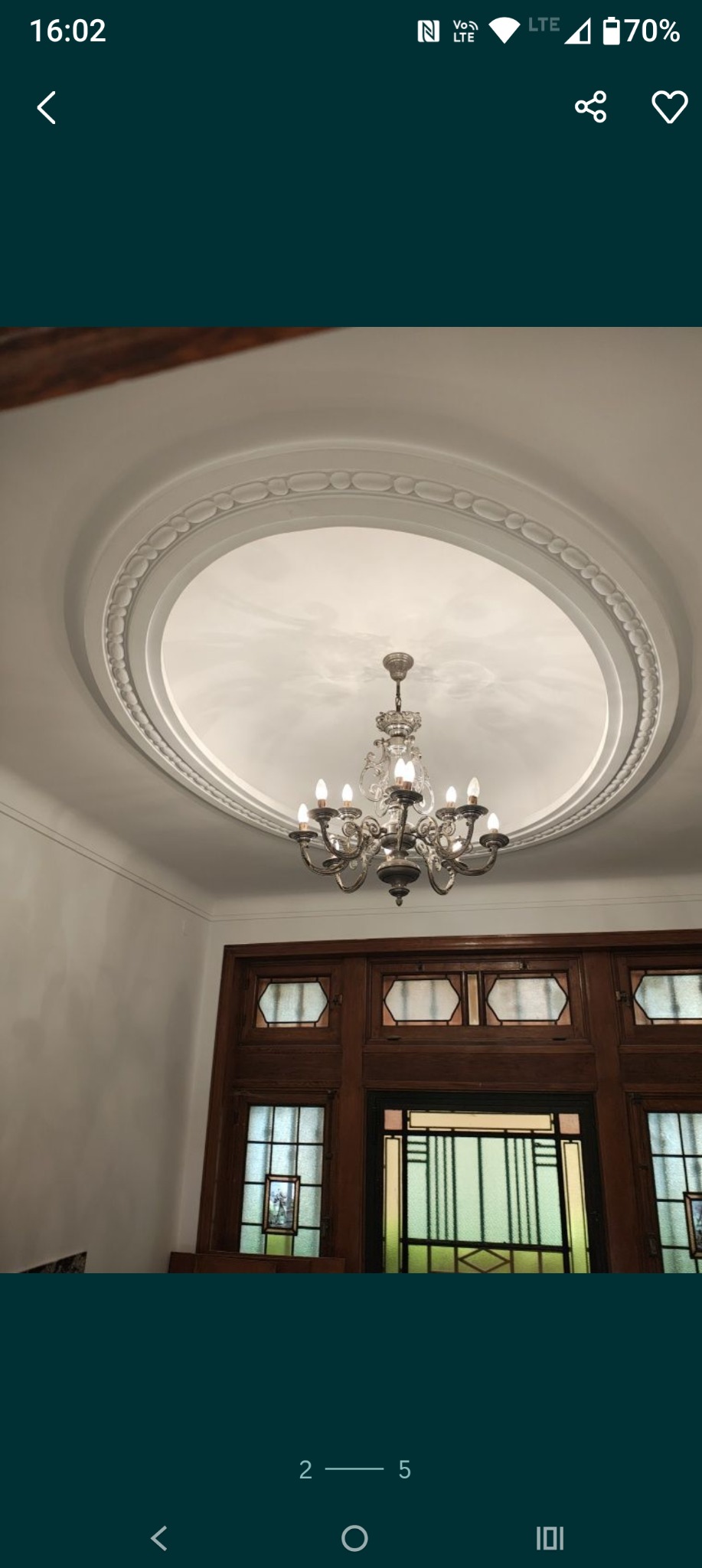 Klasyczny sufit z gładzią i dekoracyjnym okręgiem, podwieszony żyrandol. Widoczne drewniane drzwi z przeszkleniami w stylu art deco.