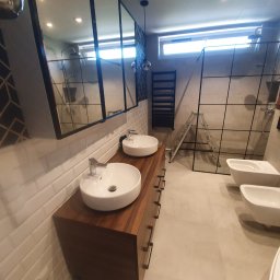 Katarzya Jarosław - Nowoczesna łazienka z dwoma okrągłymi umywalkami na drewnianej szafce, białymi kaflami na ścianach, bidetami i kabiną prysznicową z czarnymi ramami, widoczna drabinka grzejnikowa i aluminiowa drabina.