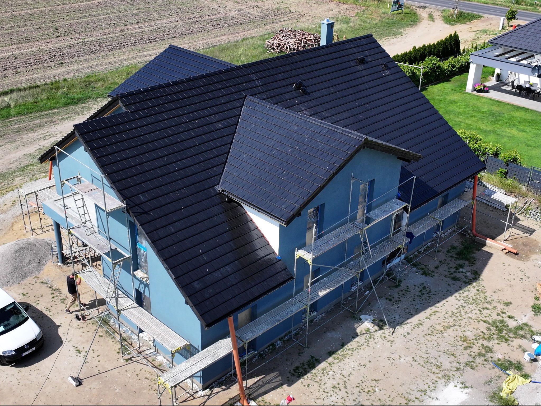 Wysoki kąt widzenia na dom murowany w trakcie budowy w Zielonej Górze, z widocznymi rusztowaniami i stertą piasku obok białego samochodu.