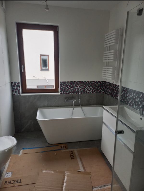 Nowoczesna łazienka w trakcie prac wykończeniowych: wolnostojąca wanna, grzejnik drabinkowy, mozaika na ścianie, zabezpieczona podłoga kartonem z logo TECE.