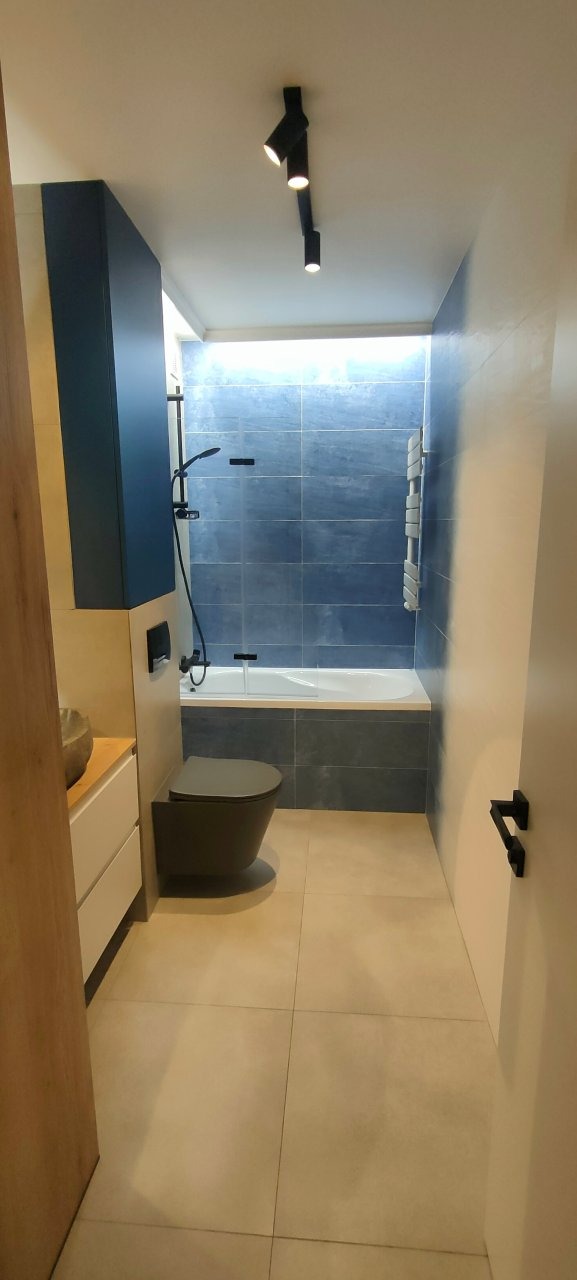 Nowoczesna łazienka w Warszawie z podwieszaną toaletą w kolorze grafitowym, kabiną prysznicową z niebieskimi płytkami i oświetleniem punktowym.