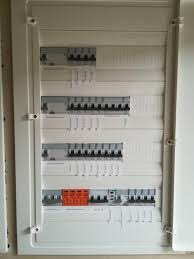 Otwarta skrzynka rozdzielcza z widocznymi bezpiecznikami i wyłącznikami, część z elementami w kolorze pomarańczowym.