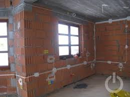 Surowy stan wnętrza z cegły ceramicznej, widoczne okno, instalacja elektryczna natynkowa w białych peszlach, puszki instalacyjne, w tle szary sufit betonowy.