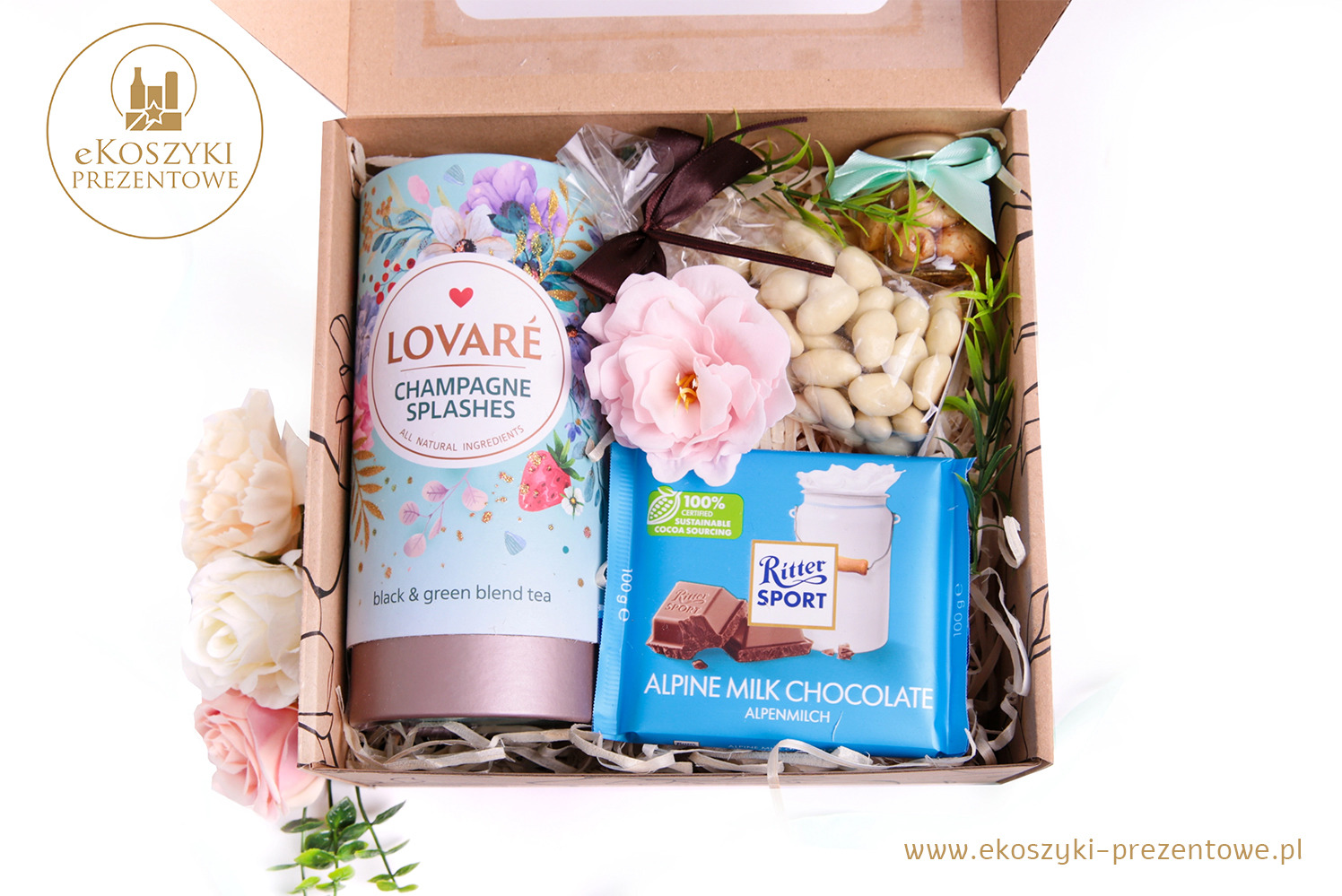 Otwarty kartonowy box z herbatą Lovare, czekoladą Ritter Sport, migdałami w lukrze i dekoracją kwiatową. Całość utrzymana w jasnej, pastelowej kolorystyce.