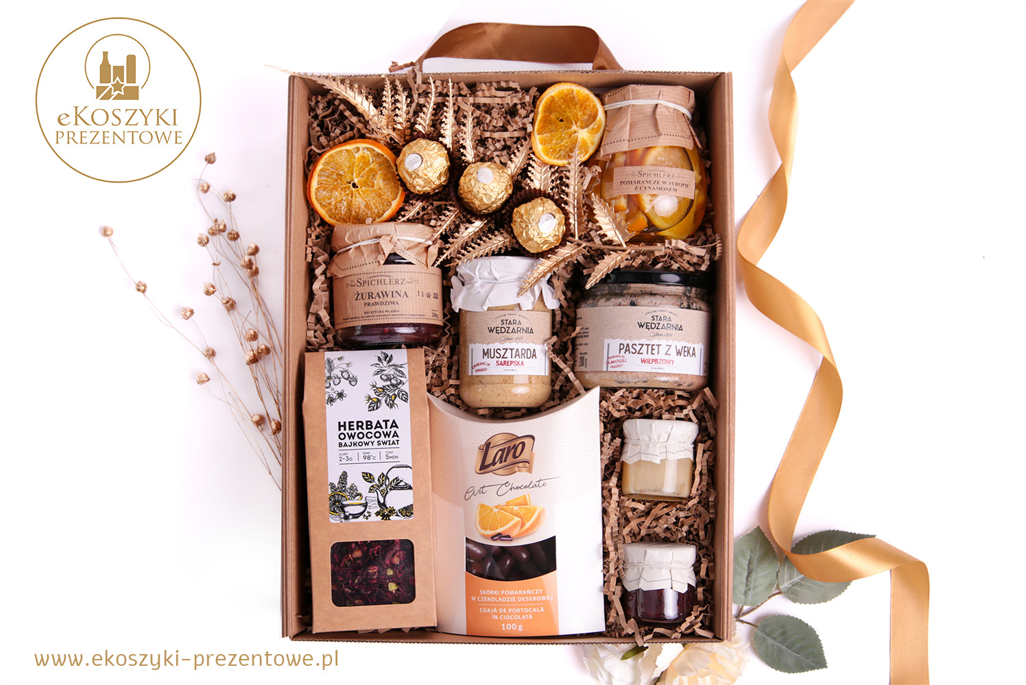 Elegancki zestaw upominkowy w kartonowym pudełku, wypełniony słoiczkami z przetworami, czekoladkami, herbatą i suszonymi pomarańczami, udekorowany wstążką.