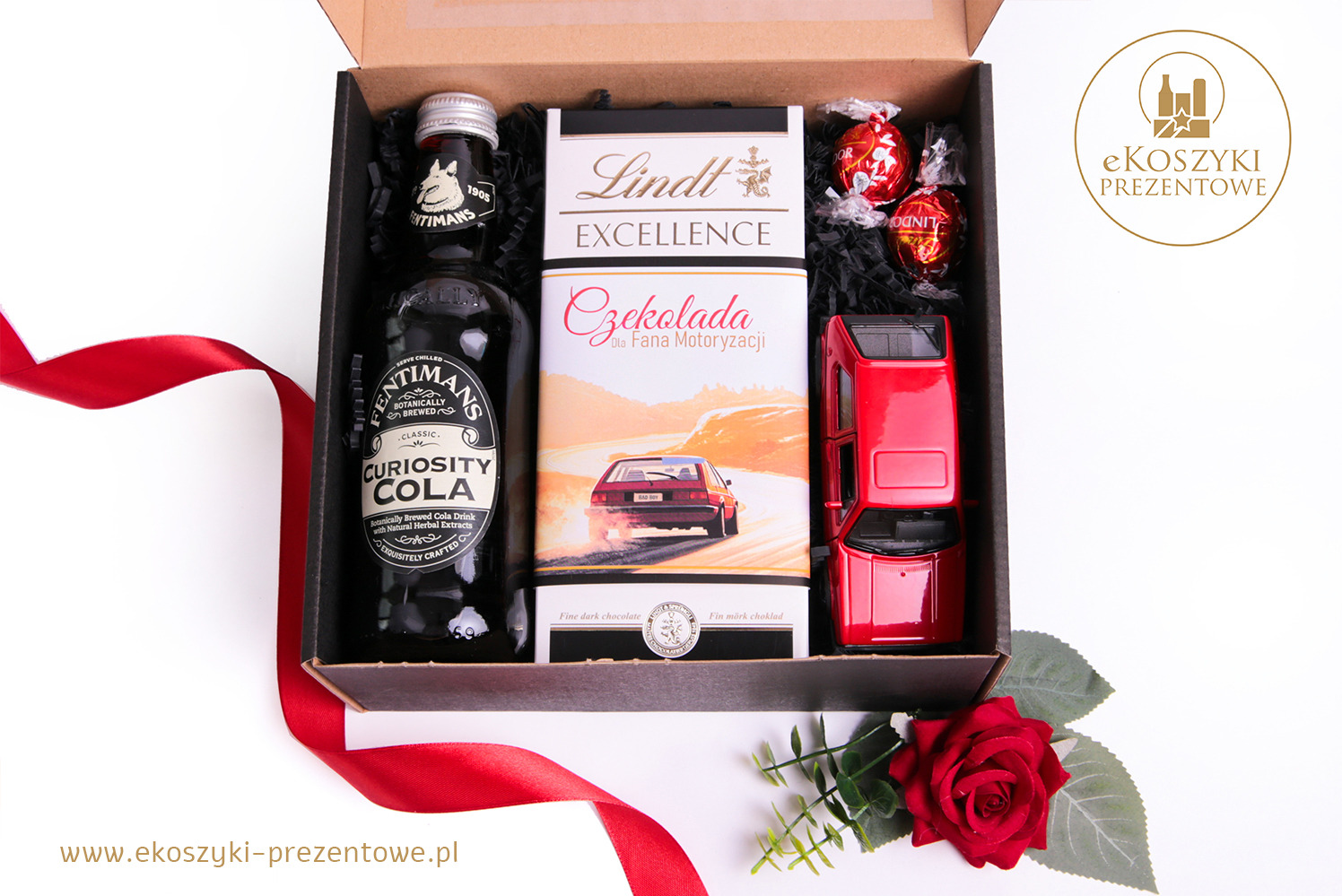 Tematyczny zestaw upominkowy: cola Fentimans, czekolada Lindt z motywem motoryzacyjnym i model czerwonego auta, ozdobiony czerwoną różą i wstążką.