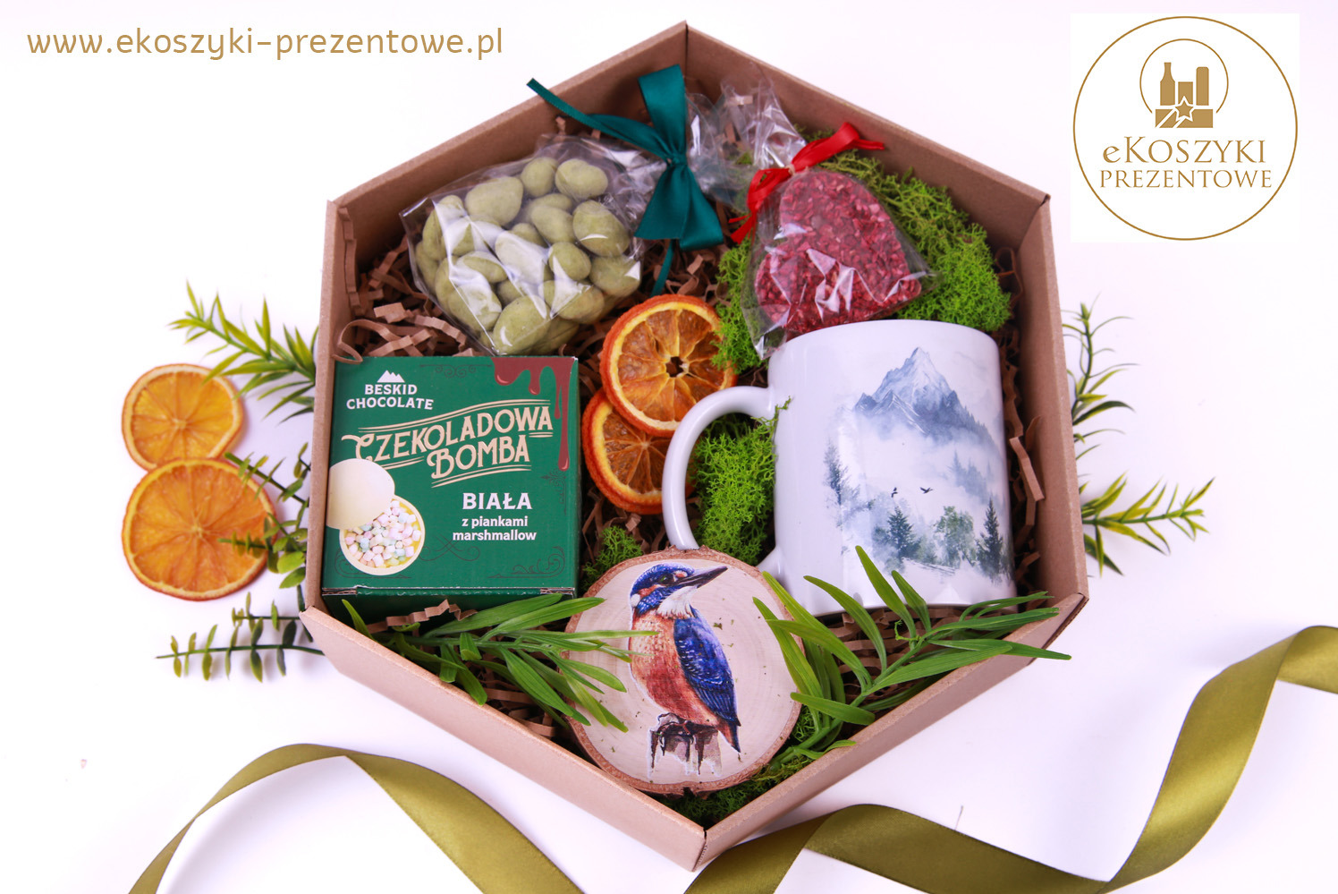 Otwarty, sześciokątny box z upominkami: czekolada, suszone pomarańcze, zielone słodycze, kubek z górskim motywem i drewniany plaster z rysunkiem zimorodka.