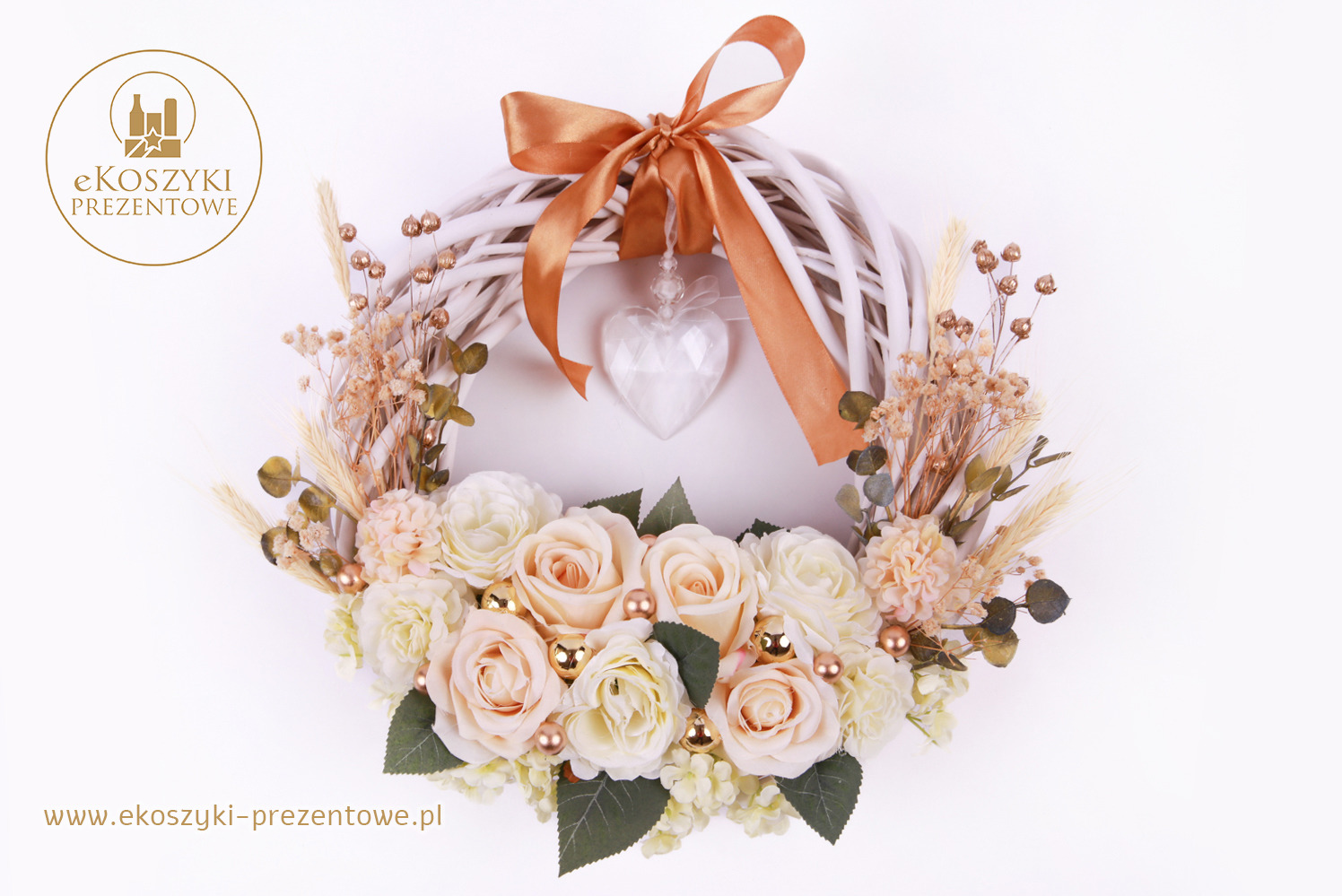 Dekoracyjny wieniec z białych gałązek, róż i złotych kulek, ozdobiony kokardą i sercem, na jasnym tle. Elegancka kompozycja.