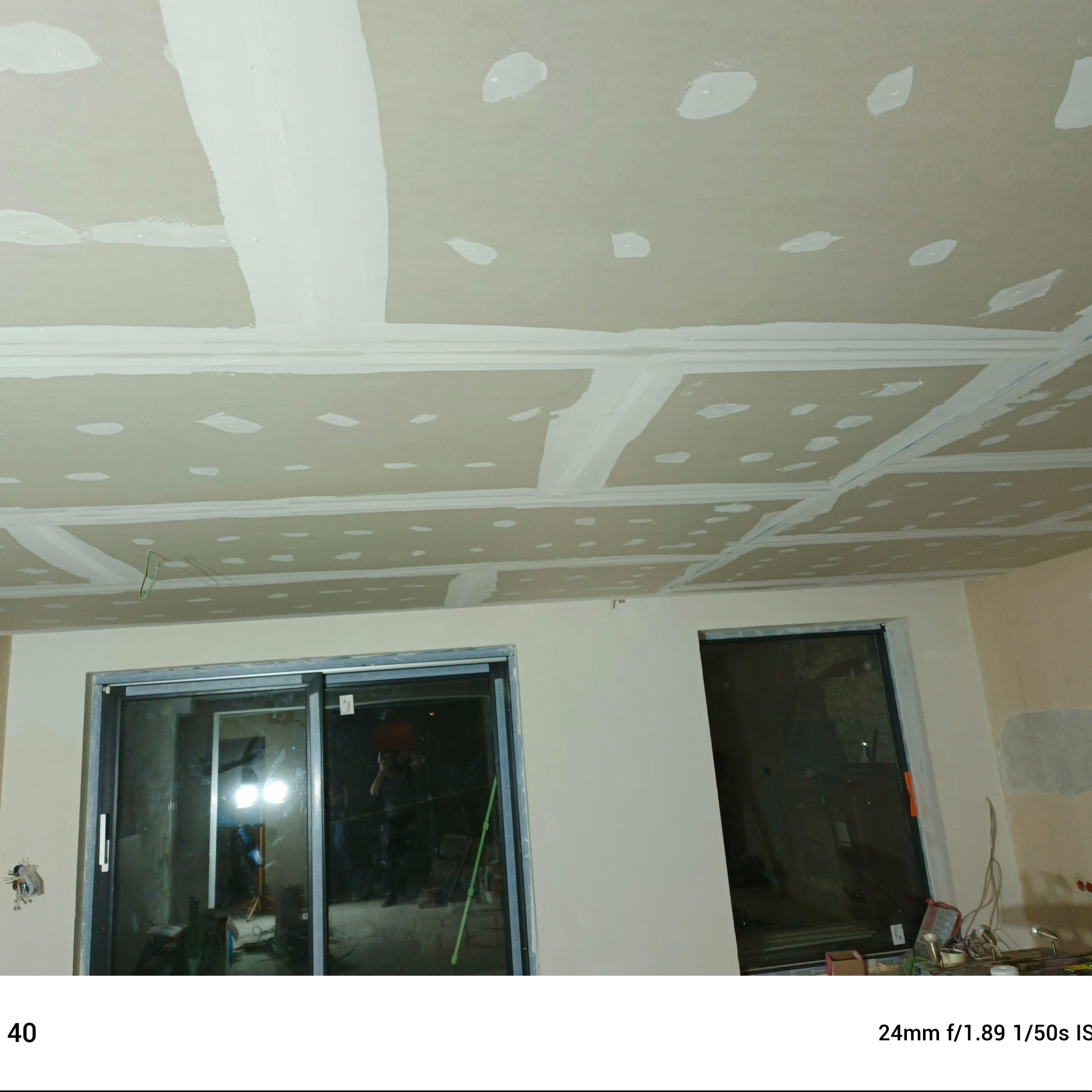 Sufit z płyt gipsowo-kartonowych po szpachlowaniu, widoczne łączenia i miejsca po wkrętach. W tle okno przesuwne i fragment ściany. Prace wykończeniowe w trakcie.