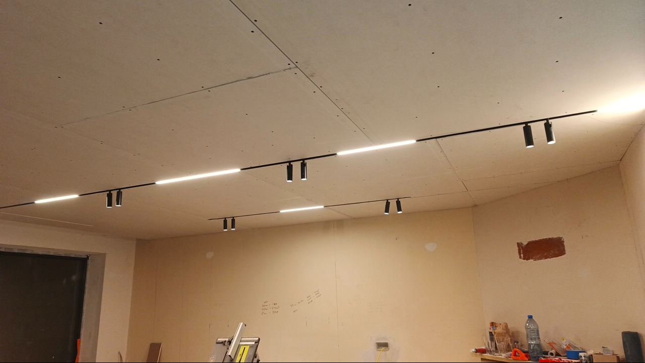 Montaż oświetlenia szynowego LED w Mordarce. Widoczne czarne reflektory i listwy na suficie z płyt gipsowo-kartonowych, ściany przygotowane do malowania.