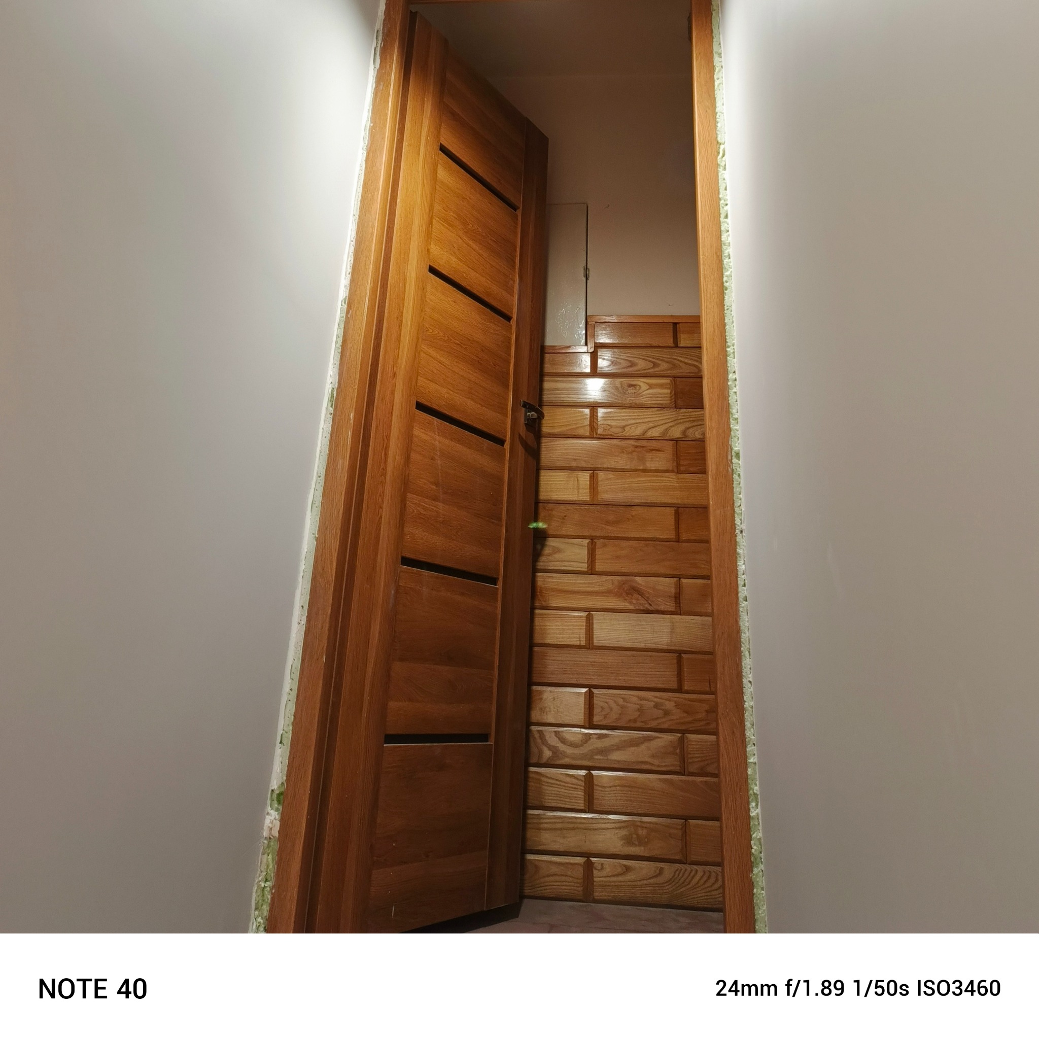 Otwarta drewniana, fornirowana  ościeżnica z widoczną ścianą wyłożoną drewnopodobną glazurą. Widoczne wypełnienie pianką montażową.