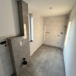 KRYSTIAN SASAL - Wnętrze łazienki w trakcie prac wykończeniowych, widoczna zabudowa stelaża WC z szarych płytek imitujących marmur, surowe ściany z przygotowanymi punktami instalacji wodnej i elektrycznej,...