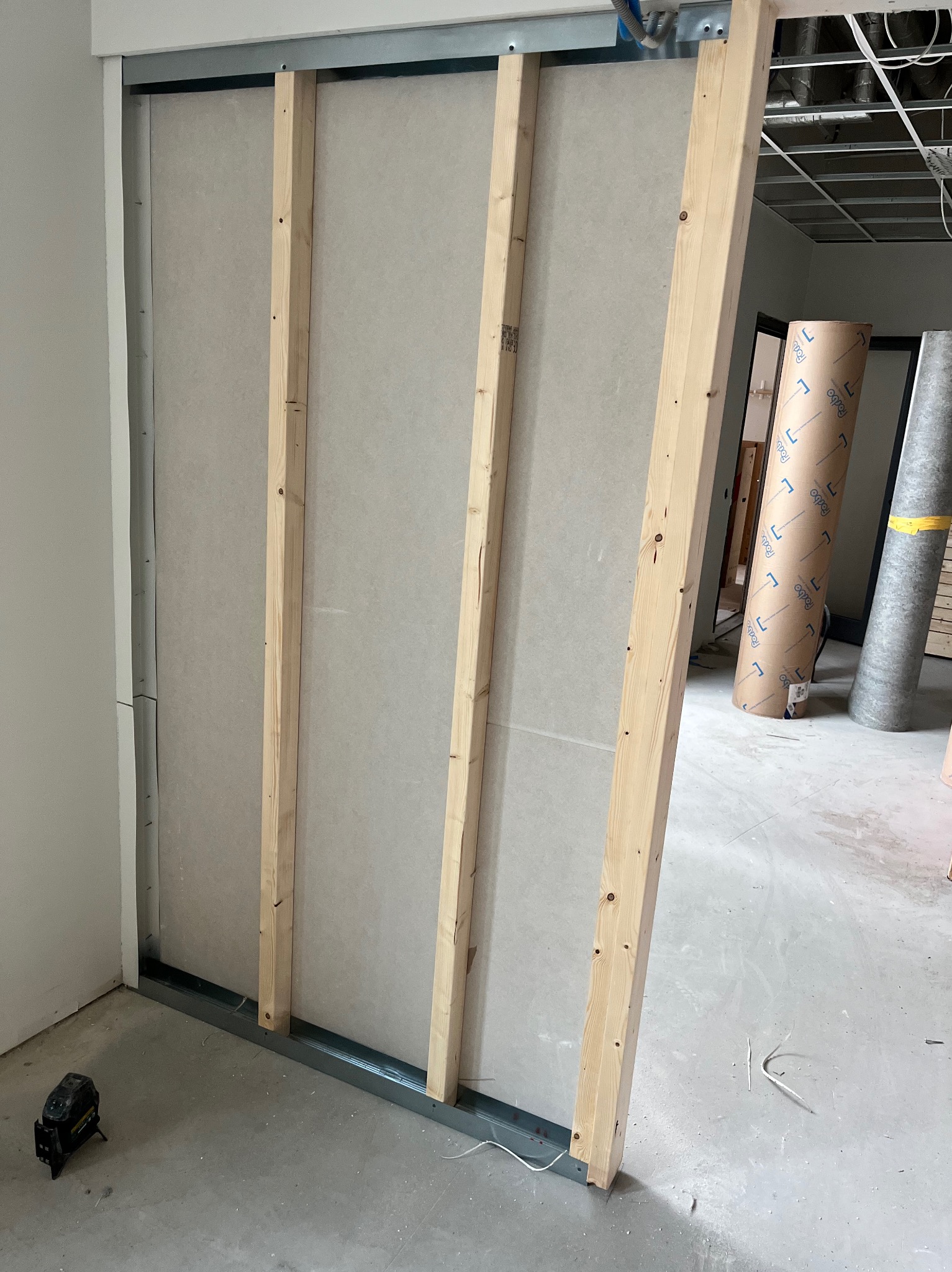 Konstrukcja ściany działowej z płyt kartonowo-gipsowych na metalowym stelażu, wzmocniona drewnianymi belkami, widoczny laserowy niwelator na podłodze.