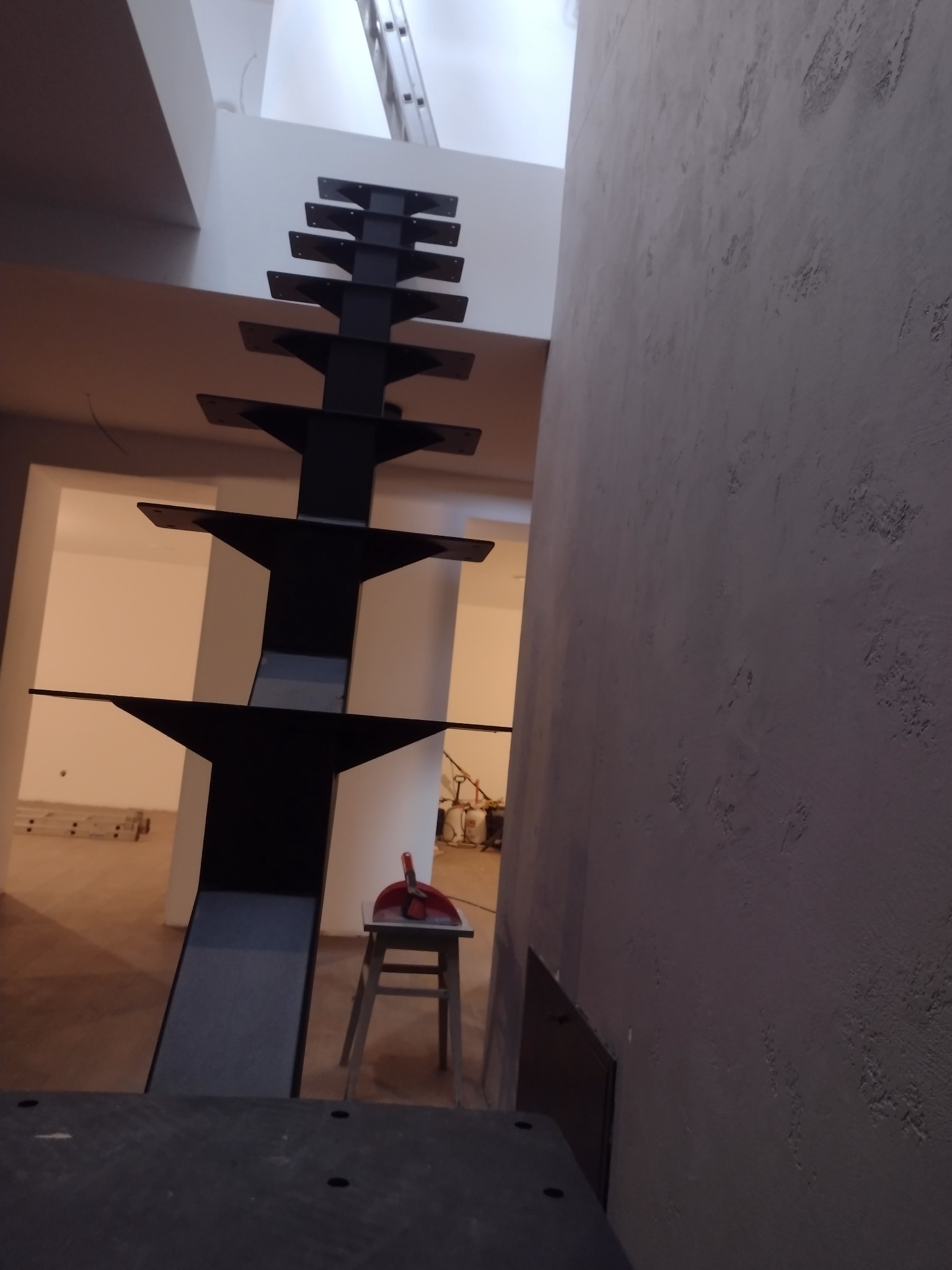 Nowoczesne schody metalowe w trakcie montażu, widok z dołu, surowa ściana, drabina w tle. Nietypowa konstrukcja schodów.