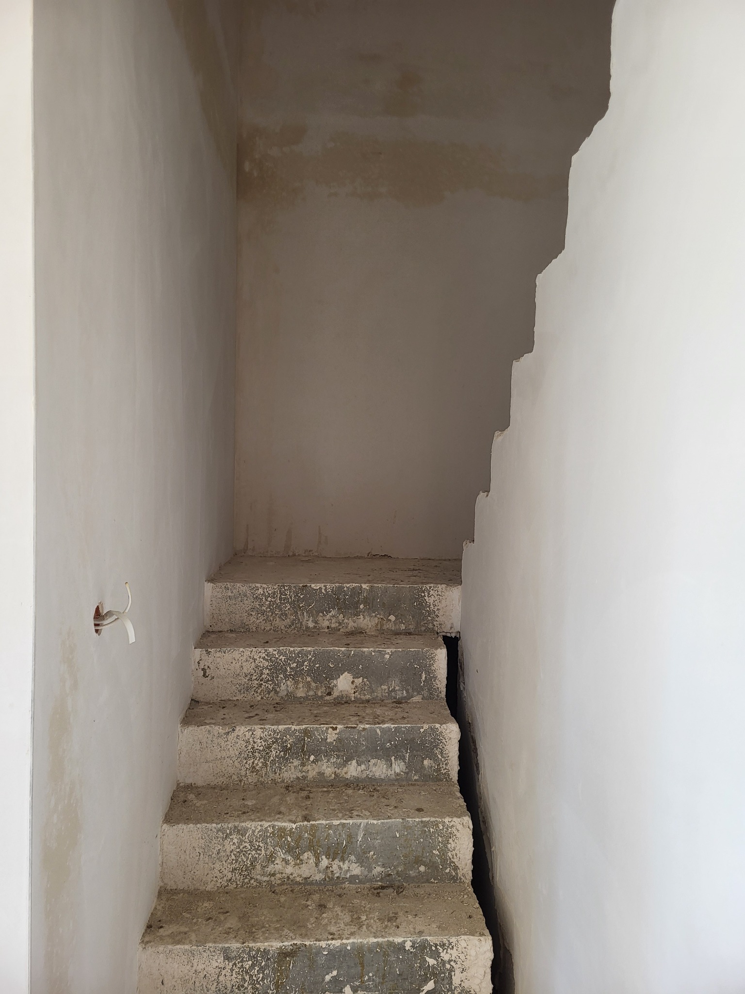 Surowe betonowe schody w trakcie prac wykończeniowych, z widoczną instalacją elektryczną w ścianie i nierównymi powierzchniami ścian przygotowanymi do dalszych prac.
