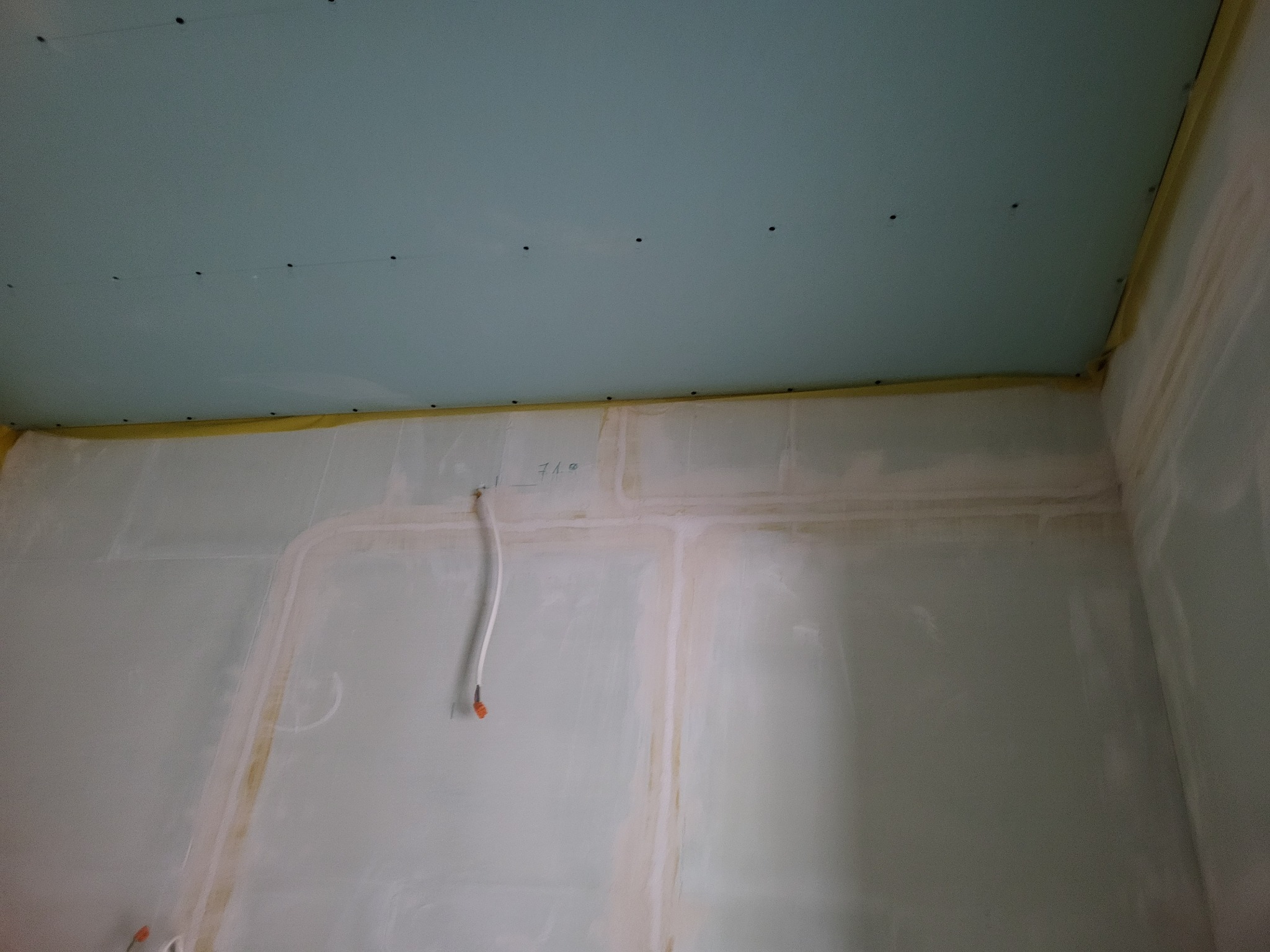 Ściana i sufit w trakcie montażu płyt kartonowo-gipsowych, widoczne profile, przewody elektryczne i taśma zabezpieczająca.