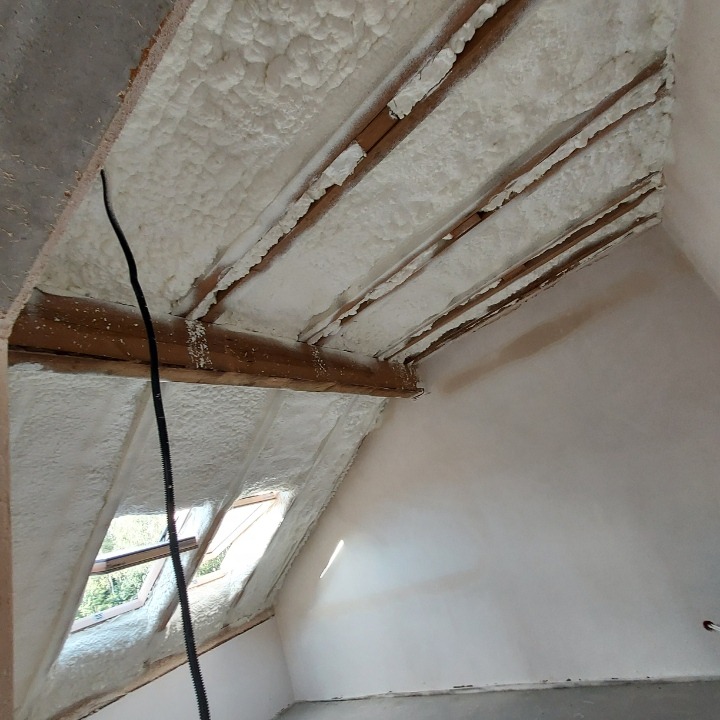 Poddasze z widocznymi krokwiami, ocieplone pianą poliuretanową, z oknem dachowym, widok od dołu.