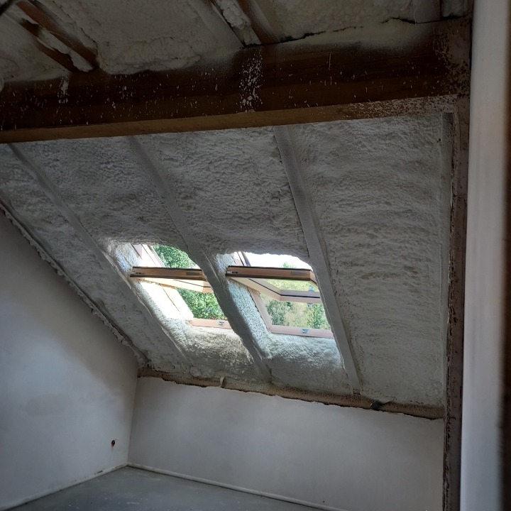 Poddasze z oknami dachowymi po izolacji pianą poliuretanową, widoczne drewniane elementy konstrukcyjne i fragment ściany przed wykończeniem.