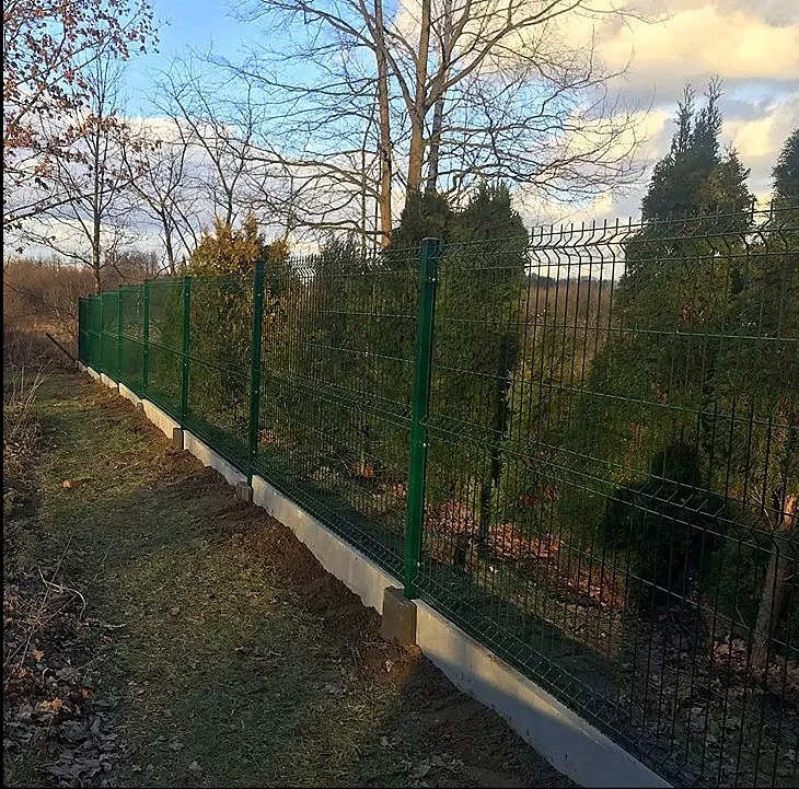 Zielony panelowy system ogrodzeniowy z podmurówką betonową, widok z boku, tło z drzewami i krzewami.